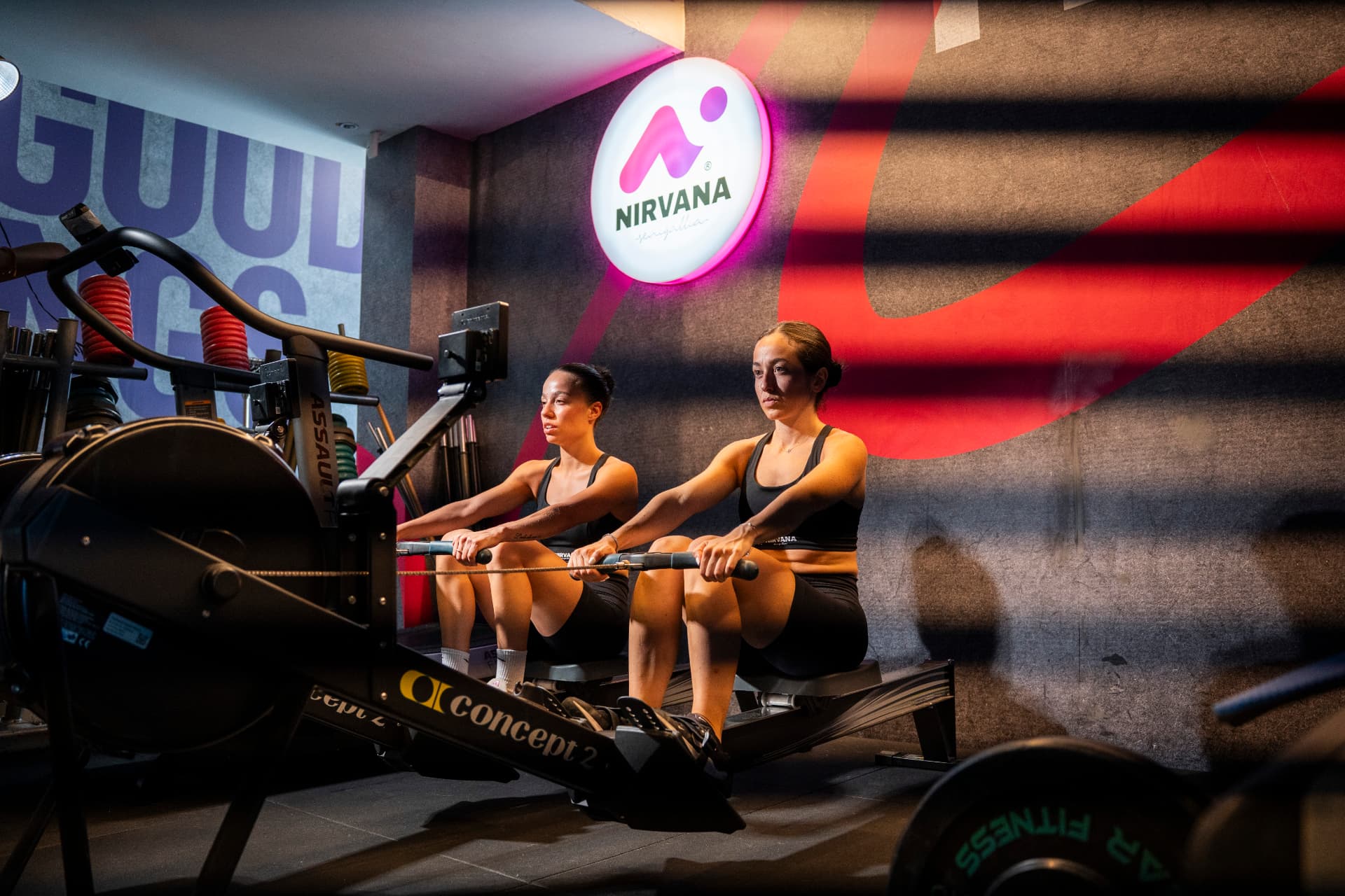 Due atlete ai vogatori nella Palestra Nirvana, con l'insegna luminosa sullo sfondo